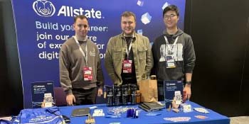 Allstate's employees standing behind Allstate's  table at the NI Developers Conference. 